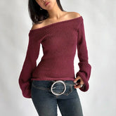 Woman wearing a burgundy off-shoulder sweater and blue jeans with a belt.
